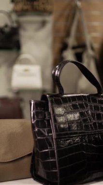 Kadın müşteri butikte şık bir deri çanta seçiyor, satın almadan önce kalite ve tasarımı inceliyor, moda mağazasında sergilenen çeşitli şık çantalar arasından seçim yapıyor. Dikey video
