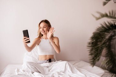 Teknoloji ve insan kavramı. Akıllı telefonlu beyaz bir kadın video çekiyor ve erkek arkadaşıyla zoom 'da el sallıyor. Boşluğu kopyala