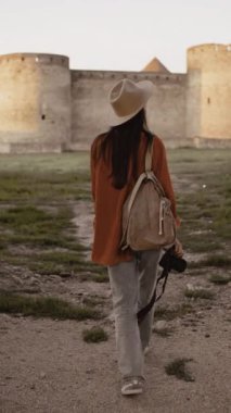 Sırt çantalı bir turist ve eski bir kalede kamerayla yürüyor. Arka görünüm