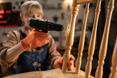 Kadın zanaatkar, evdeki atölyede elektrikli matkapla ahşap sandalyeyi monte ediyor. Boşluğu kopyala