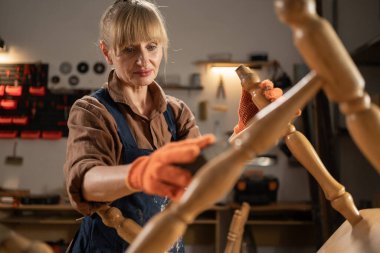 Küçük işletme, marangozluk ve başlangıç konsepti. Orta yaşlı kadın marangoz atölyede ahşap süngerle eski ahşap sandalyeyi cilalıyor. Boşluğu kopyala