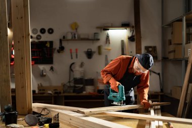 Atölyesinde odun kesmek için yapboz kullanan kadın marangoz, marangozluk projelerinde ustalık ve hassasiyet gösteriyor. Boşluğu kopyala