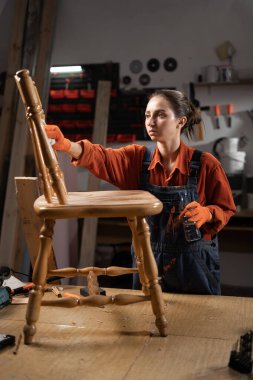 Dişi marangoz boyayı soyar. Bir atölyede ahşap sandalyenin restorasyonu. Atölyedeki tamirci. Boşluğu kopyala