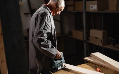 Emekli usta marangoz elektrikli yapboz kullanarak tahta kesiyor. Marangozlar çalışır. Atölyedeki marangoz. Yetenekli meslek ve yerel sanatçılar kavramı. Boşluğu kopyala