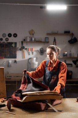 Atölyede çalışan genç bir kadın, yenilenme sürecindeki işçiliğe ve detaylara odaklanmak için koltuğun yerine kumaşı döşeyerek eski mobilyaları restore ediyor. Boşluğu kopyala