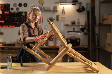 furniture restoration and diy concept. Middle aged woman in gloves with solvent to rag preparing old wooden chair for renovation. Copy space clipart