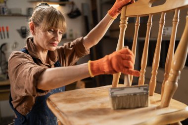 Orta yaşlı kadın marangoz, marangozluk atölyesine boya sürüyor, zanaatkar çalışıyor. Boşluğu kopyala