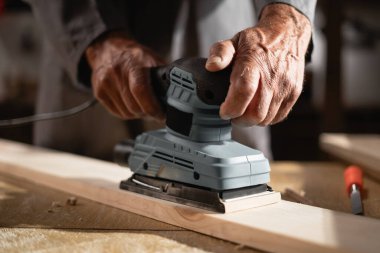 Kıdemli marangoz atölyede ahşap zımparalıyor. Kapat.