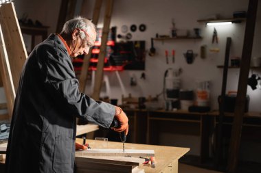 Marangoz dükkanında ahşap işlemek için elektrikli matkap kullanan marangoz. Mobilya marangozluğu ve marangozluk endüstrisi. Boşluğu kopyala