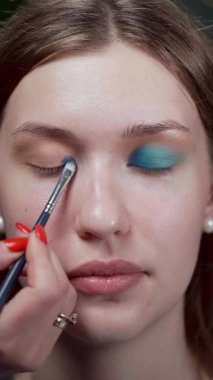 Makyaj fırçasının bir kadının kapalı gözkapağına göz farı sürerken yakın çekim görüntüsü. Detaylı çekim makyaj başvurusunda hassasiyet ve özeni vurguluyor