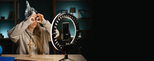 Crazy conspiracy theorist blogger woman in eyeglasses streaming live at home using smartphone and ring light, doing ok gesture like binoculars. banner. copy space