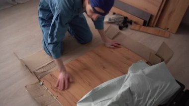 İşçi, un üzerinde oturan ahşap dolabı açan mobilya montajı yapıyor. Boşluğu kopyala