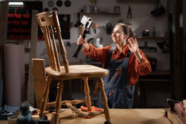 Üç ayaklı kamerayla video blogu kaydeden kadın marangoz atölyesindeki eski mobilyaları restore ediyor. Boşluğu kopyala