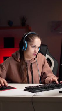 Kulaklık takan beyaz kadın oyuncu, geceleri oturma odasında öfke ve stres hissederek kişisel bilgisayarda video oyunu oynuyor. Esport oyun çevrimiçi konsepti. Dikey video