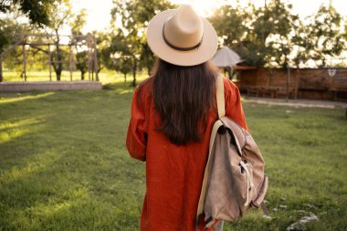seyahat ve bahar turizmi. Yeşil bahar parkında sırt çantalı, şapkalı genç bir kadın. Boşluğu kopyala