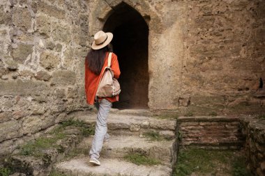 Şapka ve sırt çantası takan kadın turist eski tarihi binanın karanlık girişine doğru, macera ve miras keşfi kavramına doğru ilerliyor.
