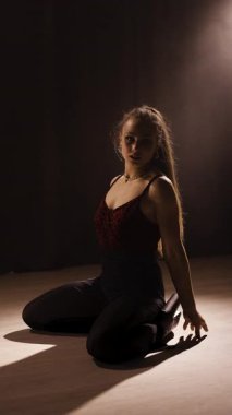 Genç, uzun saçlı kadın spor salonunda yerde striptiz dansı yapıyor. Dikey video