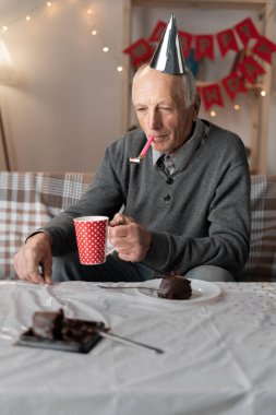 Mutsuz emekli adam, boynuzlu külah şapkalı üzgün doğum gününü kutlamak için sıkılmış bir ifadeyle başka tarafa bakıyor. Boşluğu kopyala