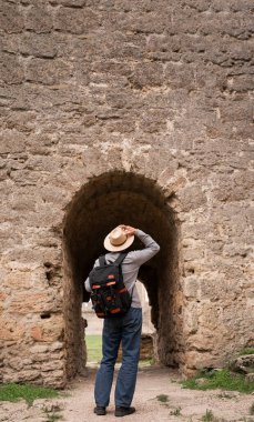 Ortaçağ kalesini ziyaret eden yaşlı bir adam sırt çantası ve dikiz aynasıyla eski taş duvarın yanında duruyor. Boşluğu kopyala