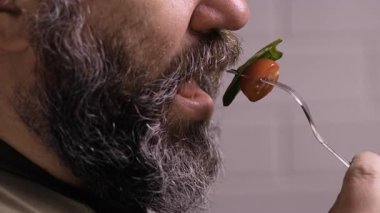 Mutfakta sebze salatası yiyen, erkek ağzı çiğneyen, tanınmamış sakallı bir adam. Yakın plan.