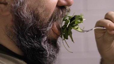 Yeşil salata yiyen sakallı adam, yakın plan. Diyet yemek ve sağlıklı yaşam tarzı konsepti. Yakın plan. yan görünüm