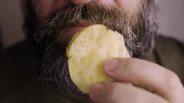 Patates cipsi yiyen şişman bir adam sağlıksız abur cuburların tadını çıkarıyor. Yakın plan.