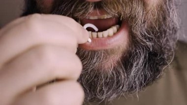 Diş ipi kullanarak diş temizleyen beyaz sakallı bir adam..