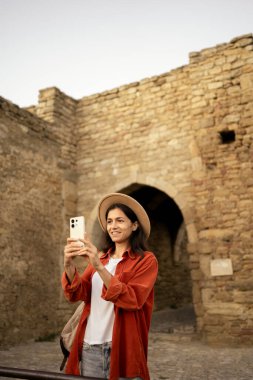 Ortaçağ kalesini ziyaret eden bayan turist akıllı telefon kullanarak selfie çekiyor. Boşluğu kopyala