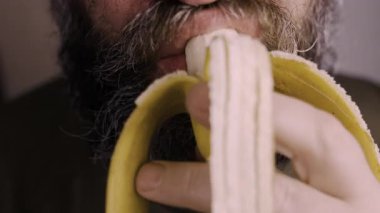Sakallı adam yüz ve ağız, çiğneyen muz meyvesi yiyor. Yakın plan. Yavaş çekim