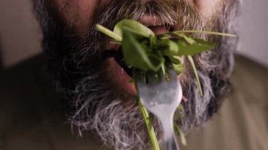 Sakallı olgun bir adam çatal tutuyor ve taze sebze salatası yiyor. Yakın plan. Evde sağlıklı bir öğle yemeği. Dengeli yemek. Boşluğu kopyala