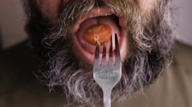 Tanınmayan sakallı adam sağlıklı salata yiyor, çataldan domates ısırıyor. Yakın plan.