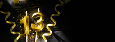 13 numara şeklinde altın bir mum, parlak konfeti ve spiral kurdelelerle çevrili karanlık bir masanın üzerinde yanarak otantik bir atmosfer yaratıyor..