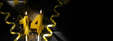 On dört numaralı altın bir mum, parlak konfeti ve spiral kurdelelerle çevrili karanlık bir masanın üzerinde yanarak otantik bir atmosfer yaratıyor..