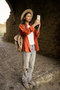 Akıllı telefon ve şapkalı turist ortaçağ kalesini ziyaret ediyor, mimari kemerler keşfediyor, bilet rezervasyonu için modern teknolojiyi kullanıyor ve seyahat ve turizmden keyif alıyor..
