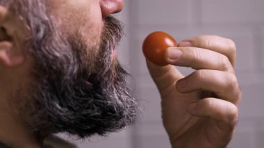 Vegan ve sağlıklı beslenme konsepti. Genç sakallı adam taze vişneli domates yiyor. Yakın plan.
