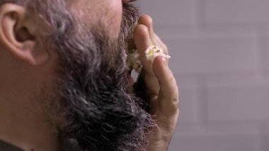 Abur cubur konsepti. Patlamış mısır yiyen sakallı adamın yakın çekimi. Ağzında tuzlu patlamış mısır. Kırpılmış görünüm