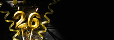 26 numara şeklindeki altın mum, parıldayan konfeti ve kıvrımlı kurdelelerle çevrili karanlık masada yanarak neşeli bir atmosfer yaratıyor. Yıl dönümü veya yıldönümü kutlaması kavramı.