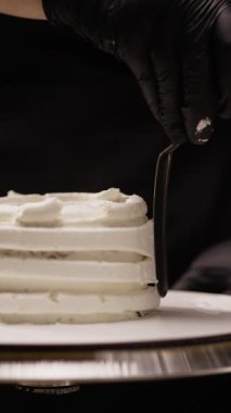 Pasta şefine yakın plan. Pasta kenarlarını kremayla yumuşatmak için spatula kullanın. Adım adım pasta hazırlama süreci, karmaşık dekorasyon becerilerinin sergilenmesi ve bitirme için ayrıntılı teknikler