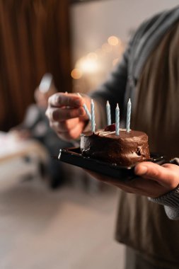 Doğum günü pastasında mum yakmak için gaz çakmağı kullanan iki adamın yakın çekimi. Evde ailenle kutlamaya hazırlanmak ve sıcak bir şenlik ortamı yaratmak..