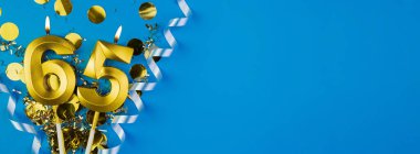 65 yıllık kutlama. Altmış beş numaralı altın yanan mumlar mavi arkaplanda konfetili, kopyalama alanı. Selamlama pankartı.