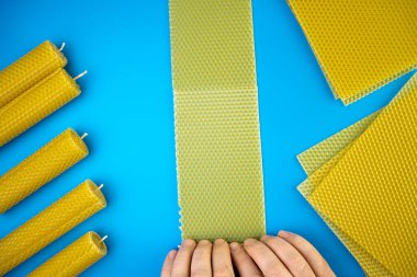 DIY ve hobi konsepti. Mavi arka planda balmumundan ev yapımı mum yapan kadın elleri, üst manzara, düz yatış