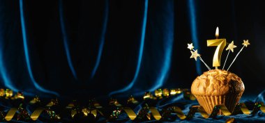 Yedinci yaş günü partisi yaklaşıyor. Kadife mavisi arka planda yedi numaralı mumu olan çikolatalı kek. Pankart, metin için boşluk.