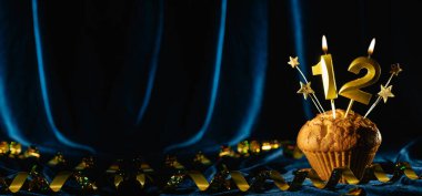 Yaş partisi 12. doğum günü. Kadife mavisi arka planda on iki numaralı mumu olan çikolatalı kek. Pankart, metin için boşluk.