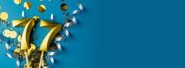 77 'inci yıl kutlaması. 77 numaralı altın yanan mumlar mavi arka planda, konfetili, kopyalama alanı. Selamlama pankartı.