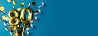 80 yıllık kutlama. Mavi arka planda, konfetili, seksen numara yanan altın mumlar, kopyalama alanı. Selamlama pankartı.