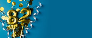 82 yıllık kutlama. Mavi arka planda konfetili 82 numaralı altın yanan mumlar, kopyalama alanı. Selamlama pankartı.