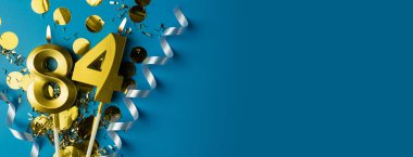 84 yıllık kutlama. Mavi arkaplanda 84 numaranın altın yanan mumları, konfeti ile, kopyalama alanı. Selamlama pankartı.