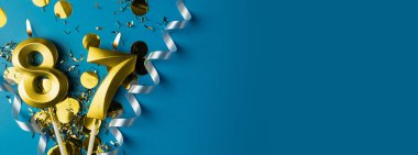 87 yıllık kutlama. Mavi arka planda konfetili 87 numaralı altın yanan mumlar, kopyalama alanı. Selamlama pankartı.