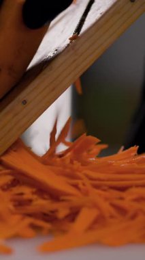 Ahşap rende taze havuç rendeleyen eldivenli şeflerin yakın çekimi. Bir diyet salatası hazırlama süreci.