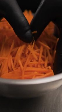 Şefin elleri siyah eldivenli, rendelenmiş havuçları metal bir kasede baharatlarla karıştırırken. Bir diyet salatası hazırlama süreci